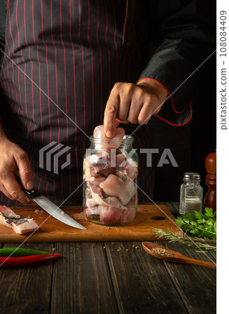 The chef puts steaks with raw fish into a jar. The concept of salting or canning fish at home with spices and coriander at home 108084409