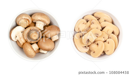 Cultivated brown mushrooms, fresh and canned slices, in a white bowl. Agaricus bisporus, or also champignons, common, button or table mushrooms. Close-up, from above, isolated over white, food photo. 108084438