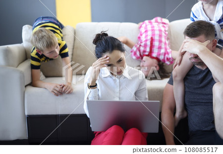 Tired man and woman are sitting on floor with laptop holding their heads with their hand behind them on couch children indulge. Tired man and woman are sitting on floor with laptop holding their heads with their hand behind them on couch children indulge. 108085517