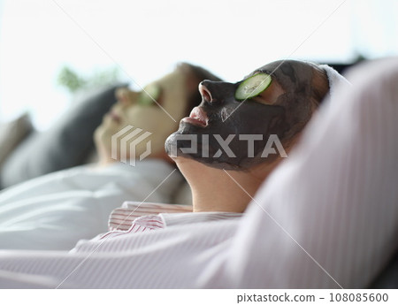 Man and woman lie with cosmetic mask on their faces and slices of cucumbers on their eyes. 108085600