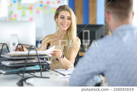 Businesswoman smiles at her colleague and takes out documents from tray. 108085659