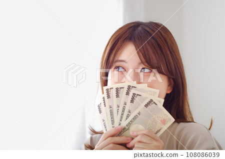 Young woman smiling and happily holding money Young woman smiling and happily holding money 108086039