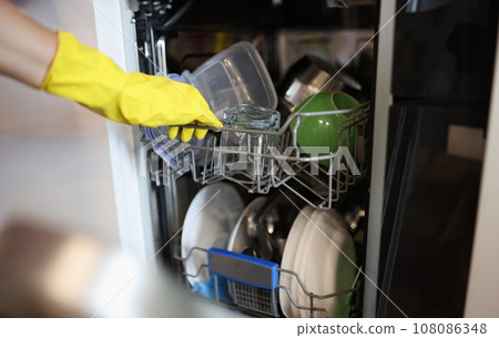 Clean dishes are taken out of the open dishwasher in yellow glove. Clean dishes are taken out of the open dishwasher in yellow glove. 108086348