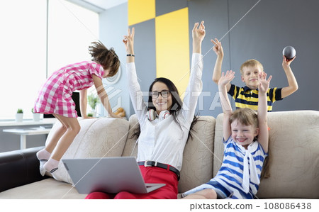 Woman, boy and two girls are sitting on couch and laughing happily and raising their hands up 108086438