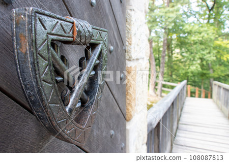 The iron knocker with the family coat of arms of an ancient aristocratic clan on the castle gate. The iron knocker with the family coat of arms of an ancient aristocratic clan on the castle gate. 108087813