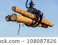 A crane with jaws loads trunks of tree, on blue backgound. 108087826