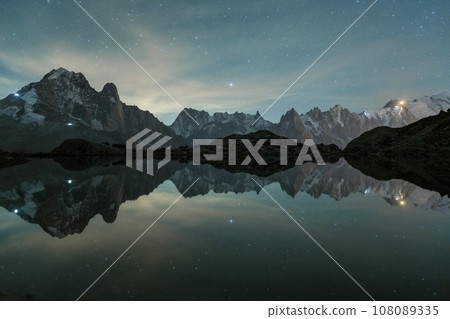Starry Sky over Mountains and Reflection in Lac Blanc Lake. Night Landscape. Aiguilles Rouges Starry Sky over Mountains and Reflection in Lac Blanc Lake. Night Landscape. Aiguilles Rouges 108089335