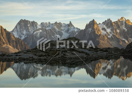 Silhouette of Hiker, Mountains and Reflection in Lac Blanc Lake at Sunset. Golden Hour. French Alps Silhouette of Hiker, Mountains and Reflection in Lac Blanc Lake at Sunset. Golden Hour. French Alps 108089338