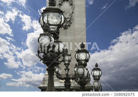 Lamp posts on Alexander III Bridge against the background of a beautiful sky with clouds. Paris, France. This arch bridge is one of the most beautiful river crossings in the world Lamp posts on Alexander III Bridge against the background of a beautiful sky with clouds. Paris, France. This arch bridge is one of the most beautiful river crossings in the world 108092075