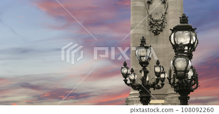 Lamp posts on Alexander III Bridge against the background of a beautiful sky at sunset. Paris, France. This arch bridge is one of the most beautiful river crossings in the world Lamp posts on Alexander III Bridge against the background of a beautiful sky at sunset. Paris, France. This arch bridge is one of the most beautiful river crossings in the world 108092260