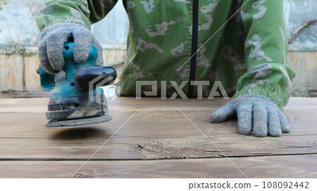 wood craftsman sands solid wood using a sander, polishing oak boards to a shine, leveling the surface of textured wood material using an emery machine 108092442