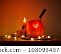 Halloween pumpkin with a comically carved face sits on a table, atmosphere is enhanced by warm 108093497