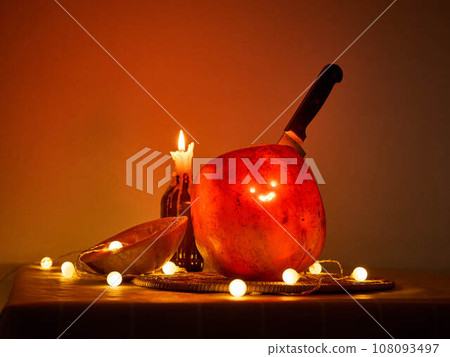 Halloween pumpkin with a comically carved face sits on a table, atmosphere is enhanced by warm Halloween pumpkin with a comically carved face sits on a table, atmosphere is enhanced by warm 108093497