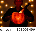 Young woman holds a comically carved Halloween pumpkin with a cute face, illuminated by a burning 108093499