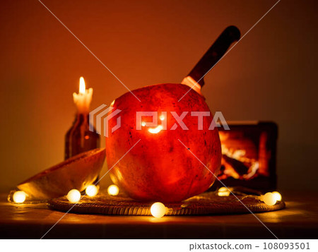 Halloween pumpkin with a comically carved face sits on a table, atmosphere is enhanced by warm 108093501