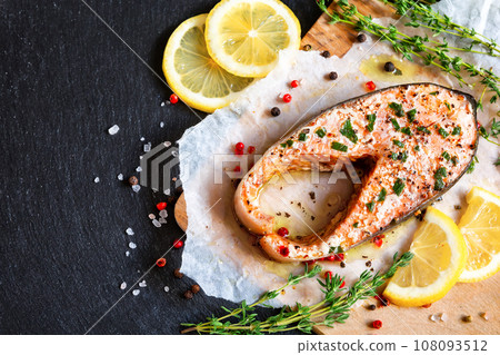 Fried salmon steak with thyme and lemon served on wooden plate on black table. 108093512