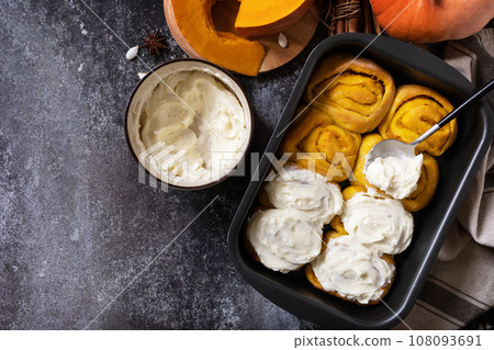 Freshly baked pumpkin cinnamon rolls or cinnabon with cream cheese on a dark stone background. Homemade seasonal autumn homemade pastry. View from above. Copy space. Freshly baked pumpkin cinnamon rolls or cinnabon with cream cheese on a dark stone background. Homemade seasonal autumn homemade pastry. View from above. Copy space. 108093691