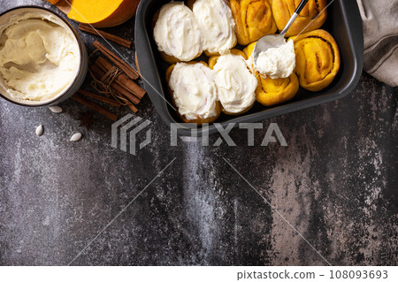 Freshly baked pumpkin cinnamon rolls or cinnabon with cream cheese on a dark stone background. Homemade seasonal autumn homemade pastry. View from above. Copy space. 108093693