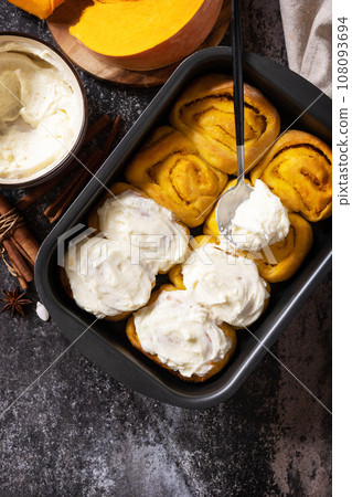 Homemade seasonal autumn homemade pastry. Freshly baked pumpkin cinnamon rolls or cinnabon with cream cheese on a dark stone background. View from above. Copy space. Homemade seasonal autumn homemade pastry. Freshly baked pumpkin cinnamon rolls or cinnabon with cream cheese on a dark stone background. View from above. Copy space. 108093694