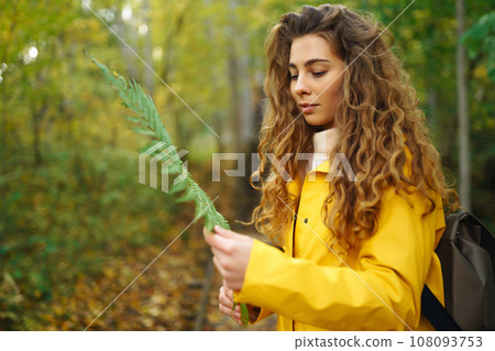 Woman in a yellow coat with backpack walks along wooden staircase, enjoying autumn scenery in forest 108093753