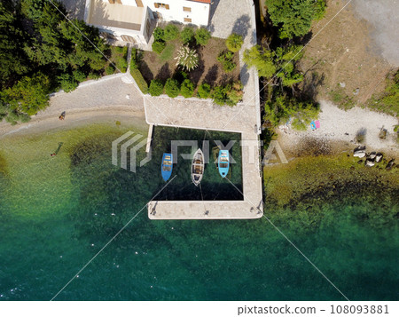 Aerial top down view of three fishing boats parked by the pier on the tropilal seashore. Drone flying over shoreline and sea surface with transparent turquoise water with sun reflections. 108093881