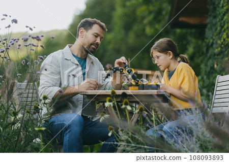 Father supporting daughter in pursuing robotics, science, IT technologies and programming. Young girl assembling a simple robot and her dad helping her. 108093893