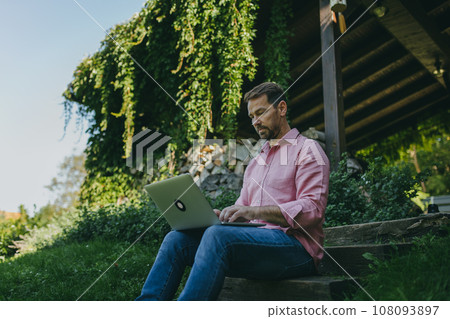 Low angle shot of man working outdoors in the garden, with laptop on legs. Businessman working remotely from homeoffice, thinking about new business or creative idea. 108093897
