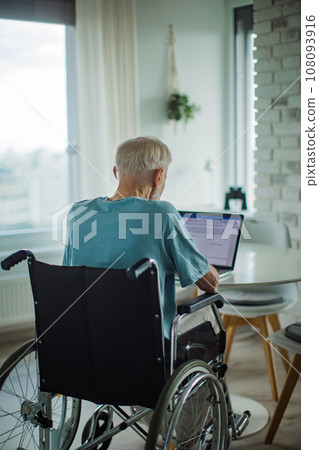 Senior man in a wheelchair write document on laptop. Elderly man using digital technologies, working on a notebook. Concept of seniors and digital skills. Senior man in a wheelchair write document on laptop. Elderly man using digital technologies, working on a notebook. Concept of seniors and digital skills. 108093916