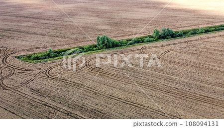 An old irrigation canal overgrown with trees among a wheat field, aerial view. Dry irrigation canal in the field, landscape. 108094131