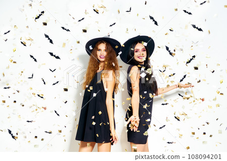 portrait of two happy young women in black witch halloween costumes. firecrackers in the background. 108094201