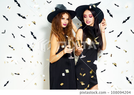 portrait of two happy young women in black witch halloween costumes. firecrackers in the background. 108094204