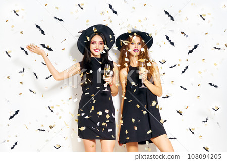 portrait of two happy young women in black witch halloween costumes. firecrackers in the background. 108094205