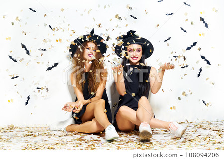 portrait of two happy young women in black witch halloween costumes. firecrackers in the background. 108094206