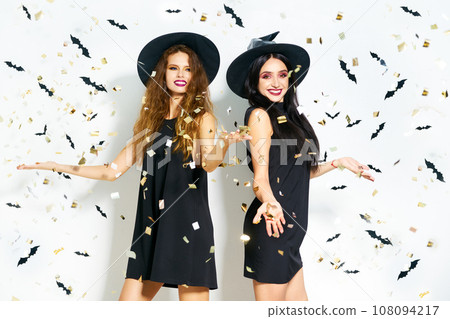 portrait of two happy young women in black witch halloween costumes. firecrackers in the background. portrait of two happy young women in black witch halloween costumes. firecrackers in the background. 108094217