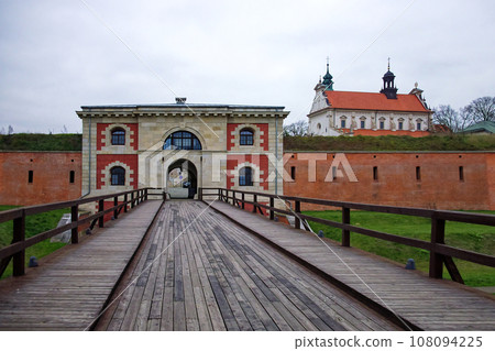 New Lublin Gate in the old Polish town of Zamosc, autumn day. Long wooden bridge over the moat. An ancient fortress wall. Ancient European architecture. 108094225
