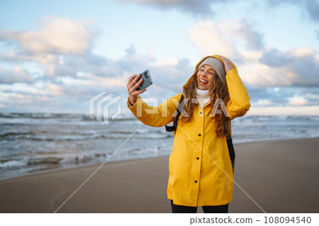 Tourist with phone. Selfie time. Tourist in yellow jacket posing by sea at sunset. Travelling. Tourist with phone. Selfie time. Tourist in yellow jacket posing by sea at sunset. Travelling. 108094540