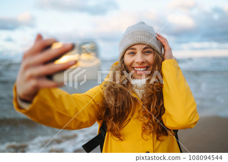 Tourist with phone. Selfie time. Tourist in yellow jacket posing by sea at sunset. Travelling. 108094544