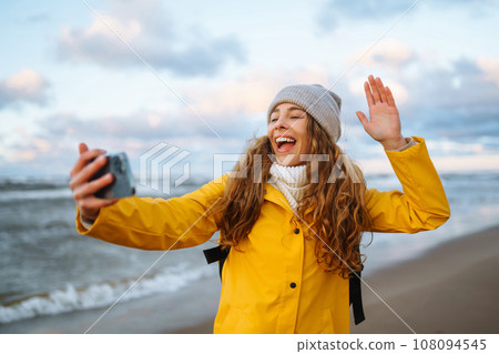 Tourist with phone. Selfie time. Tourist in yellow jacket posing by sea at sunset. Travelling. 108094545