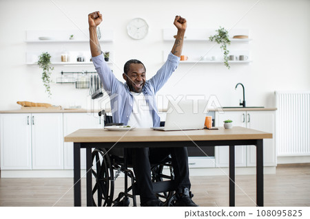 African wheelchair user celebrating success by raising hands up 108095825