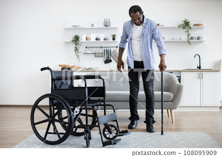 African man with disability using walking stick when raising from wheelchair 108095909