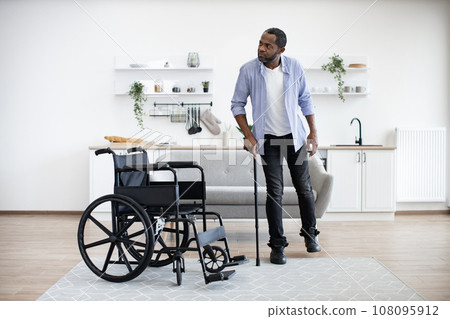 African man with disability using walking stick when raising from wheelchair 108095912