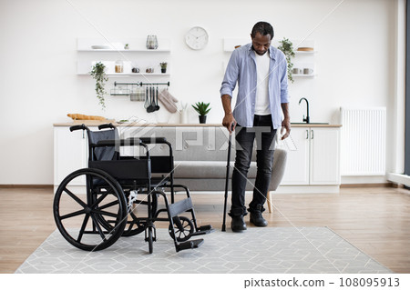African man with disability using walking stick when raising from wheelchair 108095913