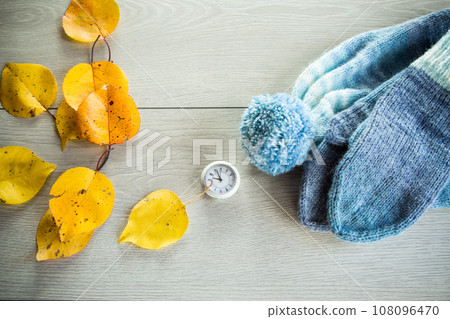 Autumn foliage, winter mittens and a clock on a wooden table. 108096470