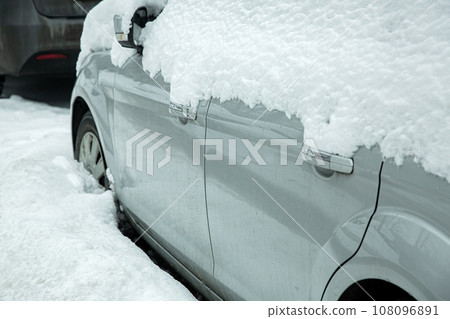 car side with folded rearview mirror with turn signal and car doors with chrome handles covered with snow on a snowy winter day, vehicle and road is covered snowdrift. car side with folded rearview mirror with turn signal and car doors with chrome handles covered with snow on a snowy winter day, vehicle and road is covered snowdrift. 108096891