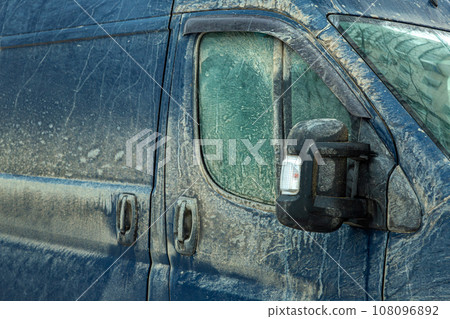 a cargo van covered in a layer of dirt, the front door with a window and a mirror with a turn signal splattered mud, close up detail of vehicle. a cargo van covered in a layer of dirt, the front door with a window and a mirror with a turn signal splattered mud, close up detail of vehicle. 108096892