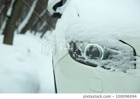 car headlight with lens xenon light covered with snow in winter weather, snowdrifts on the road. close-up of a vehicle detail. car headlight with lens xenon light covered with snow in winter weather, snowdrifts on the road. close-up of a vehicle detail. 108096894