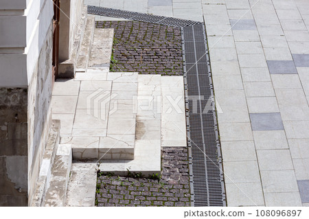 corner of a building with stools at the entrance to an old crumbling building next to a stone sidewalk in sunny weather, close-up of architecture. corner of a building with stools at the entrance to an old crumbling building next to a stone sidewalk in sunny weather, close-up of architecture. 108096897