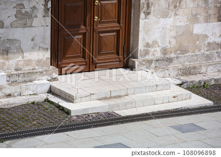 brown wooden entrance door of an white old stone building on a sunny day, close-up architecture of the old city, nobody. 108096898