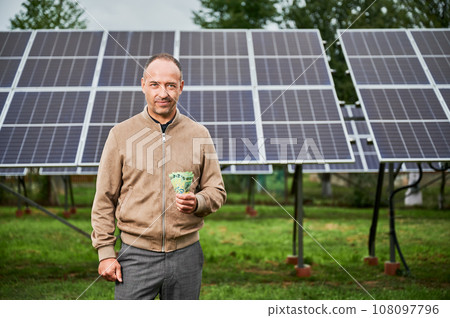 Knowledgeable man showing money he earning by investing in green energy. Promising industry of alternative energy sources. Male glad of his decision to invest in modern resources. 108097796