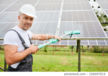 Man cleaning solar PV panel using mop. Professional worker doing good job at cleaning solar panel from dust. Man holding mop and smiling straight to camera. 108097819